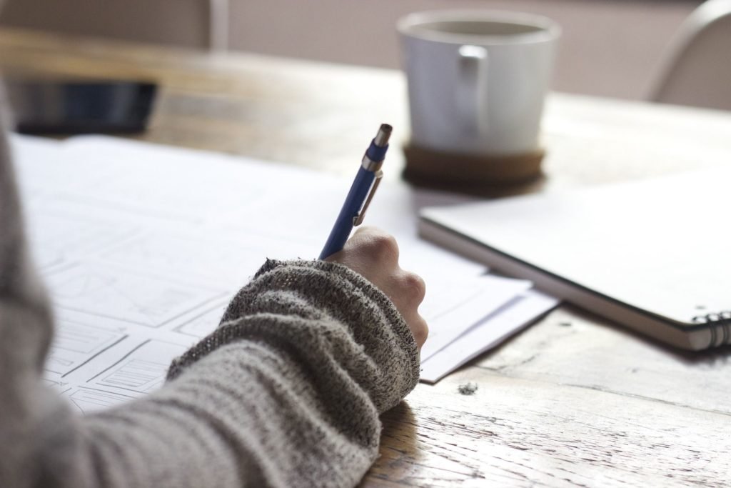 a hand writing on multiple sheets of paper, on a wooden desk