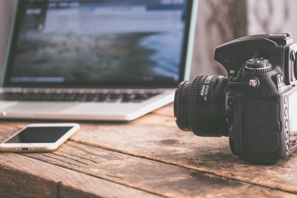 Macbook, Nikon camera, and iPhone sitting on a rustic desk 