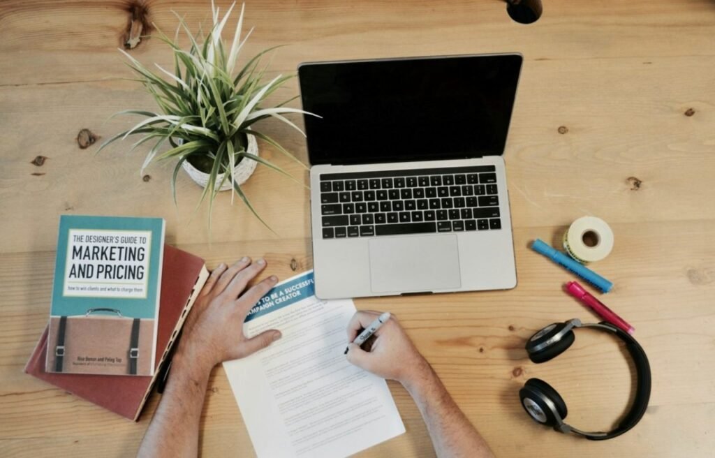 person using notepad and pen in front of laptop
